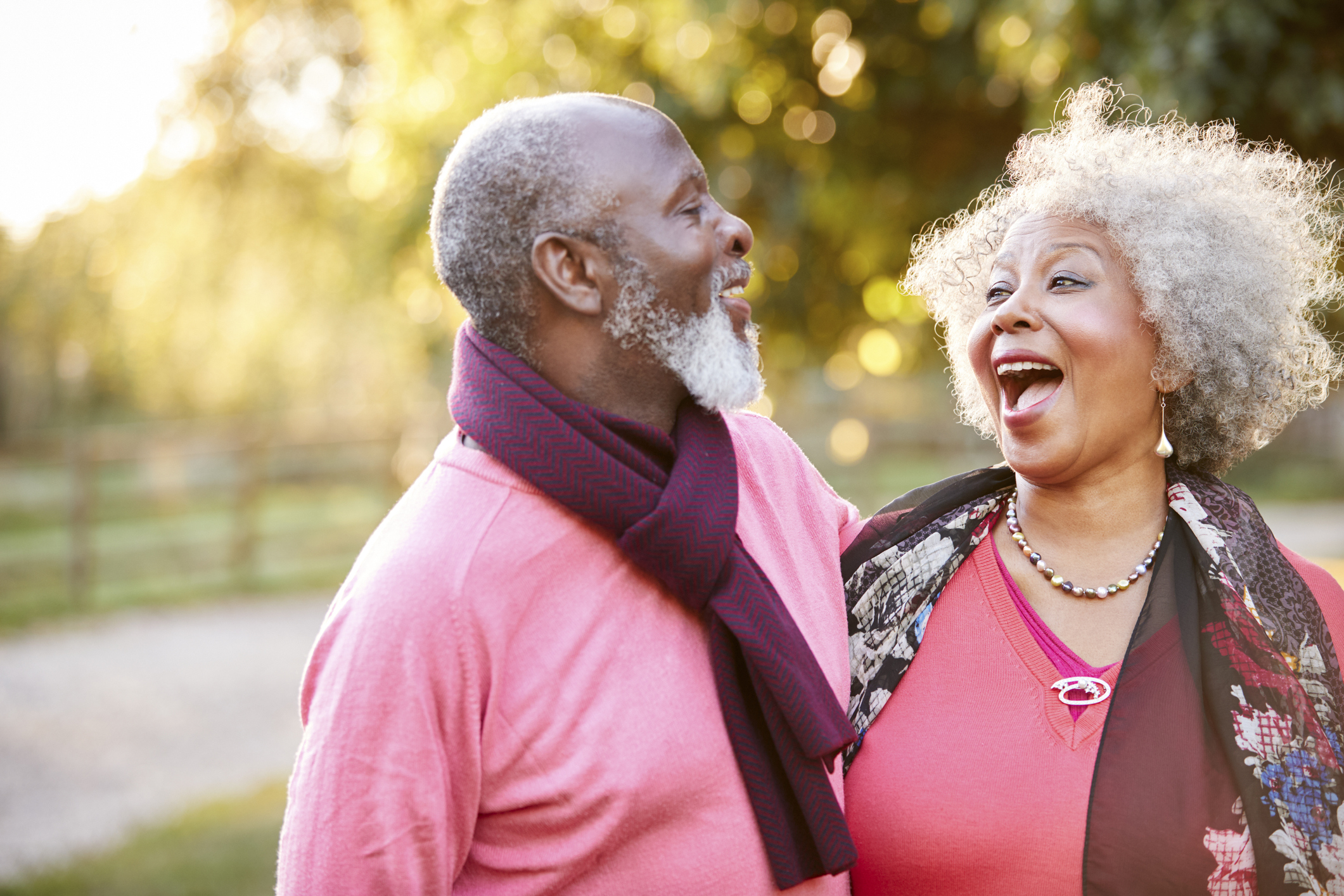 Two people wearing red, smiling at each other in front of a tree.