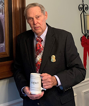 Photo of Allen Ezell wearing a suit and red floral tie while holding a ceramic mug.