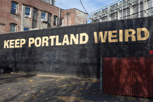 "Keep Portland Weird" painted in gold on a black wall. 