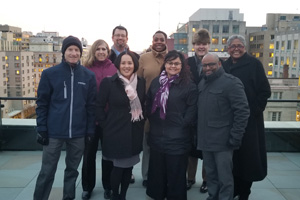 nine people wearing winter clothing pose for a photo on a rooftop