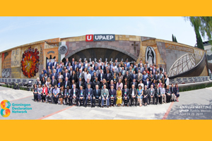 Large cohort of people pose for a photo in front of a concrete overpass 