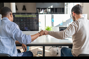 two males fist-bump as they sit next to one another working on camputers