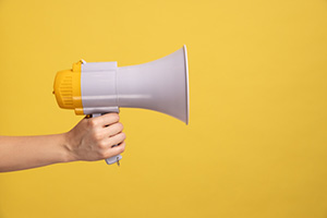 Individual holding a megaphone on a yellow background.