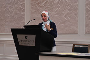 female wearing a hijab speaks from behind a podium 