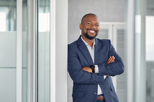 Smiling black man in navy suit leaning against doorway with arms crossed