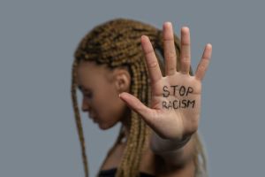 Young African American woman standing sideways, head down, showing palm with stop racism lettering