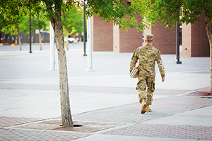 Military-connected student walking on campus with books in hand.