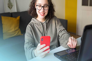 female smiling at her phone while sitting in front of her laptop