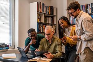 Group of individuals sharing knowledge on a tablet.