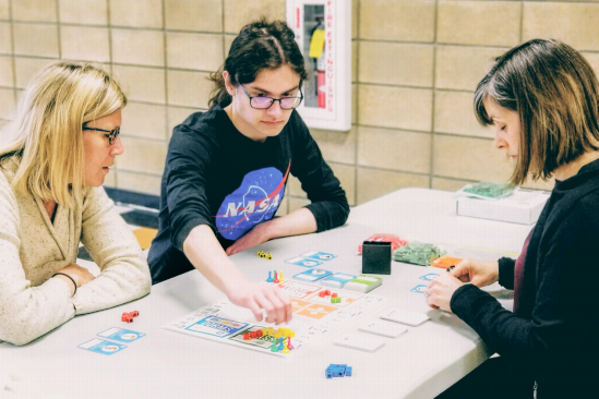 three individuals sit around a table while playing a board game
