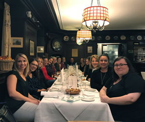 a group of several people sit on either side of a dinner table while smiling at the camera