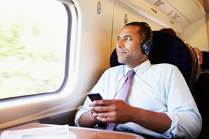 male passenger in business attire wearing headphones looks out the window of the train