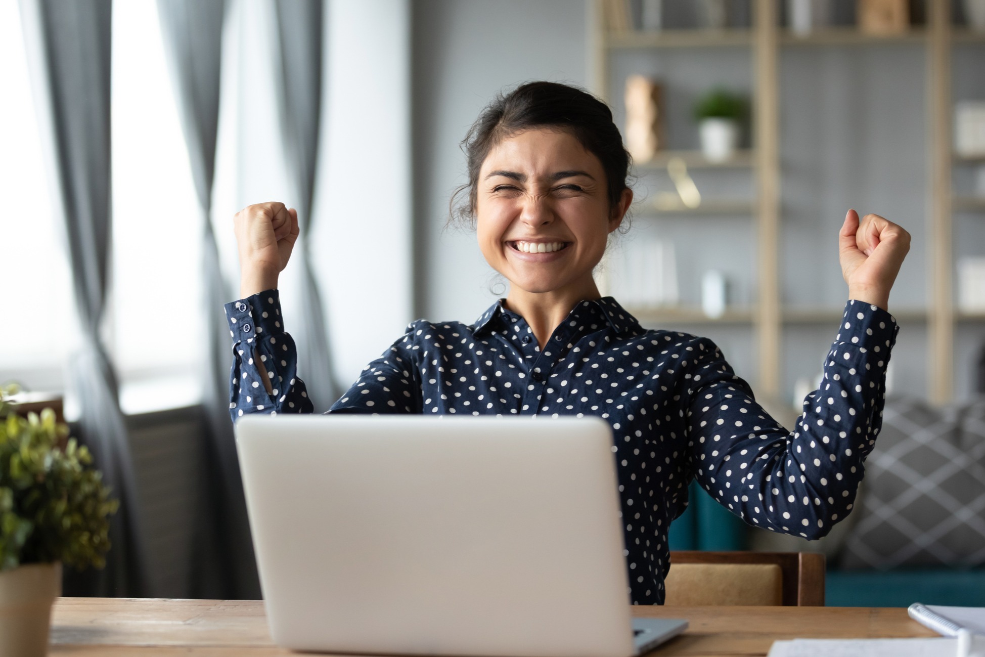 female smiling and clenching her fists in excitement as she shits in front of a laptop