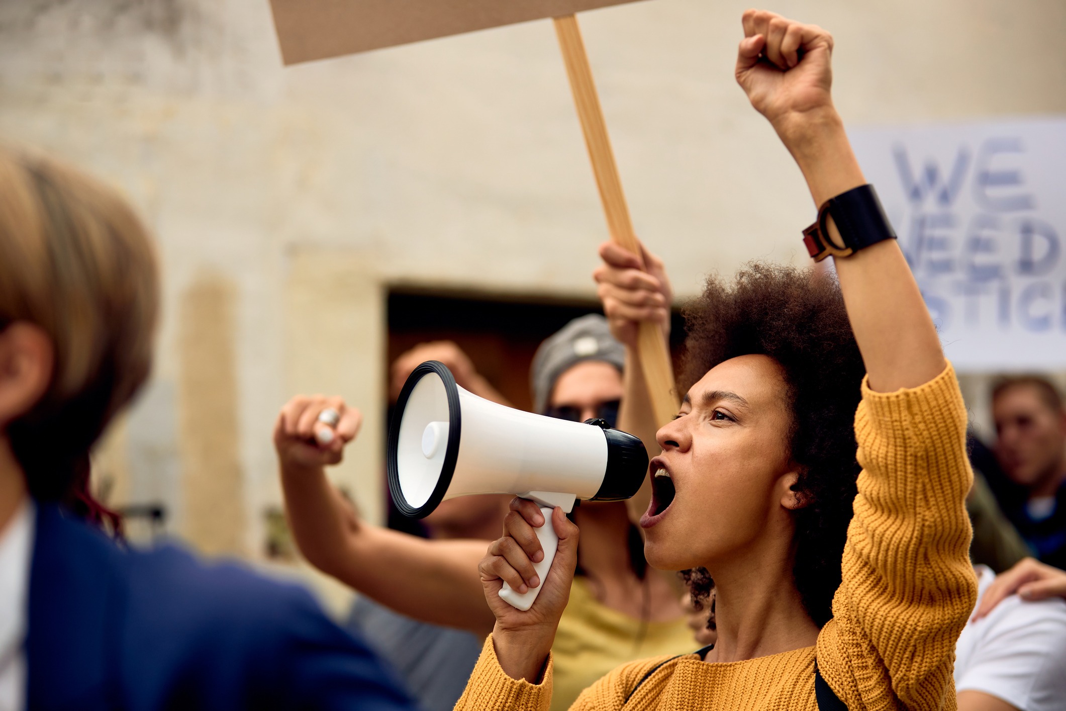 woman of color raises her fist in the air while using a bull horn during a protest