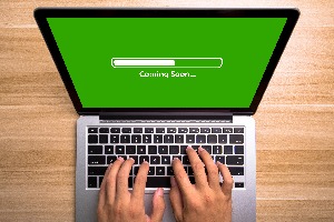 person typing on a laptop displaying a green screen with a progress bar at about 50%