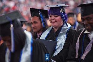 female with purple hair smiles while wearing graduation cap and gown