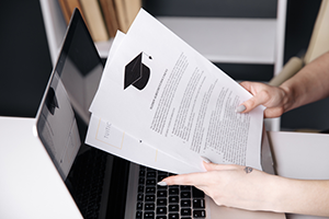 Individual holding fafsa papers in front of a laptop.