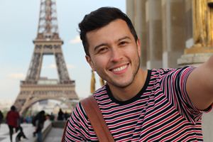 male student smiles for a selfie in front of the Eiffel tower