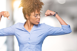 Female of color flexes biceps in a blue dress shirt