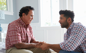 younger male comforts an older male, who is crying, by holding his hands