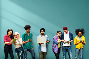 diverse group of people stand in front of a solid turquoise-green background and look at various mobile devices together