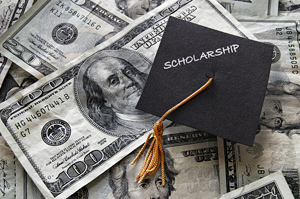 scattered 100 and 20 dollar bills with a graduation cap, displaying the word "scholarship", on top