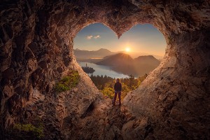 figure stands in the heart shaped entrance to a cave looking out on nature