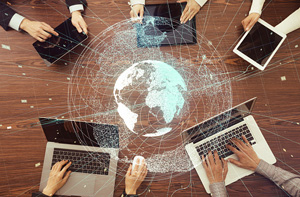 five people working in a circle on their laptops/tablets with a globe hologram in the middle