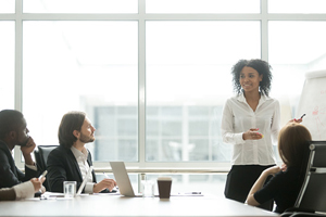 smiling female stands and present to 3 others who are seated