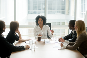 female sits at the head of a table and speaks to a group of 4 people