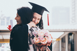 person wearing graduation gown and cap hugs a female