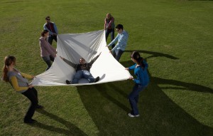 group of people in a green field catch someone with a large blanket