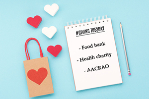on a blue table covered with red and white hearts, a notepad reads "giving tuesday" with a list below: food bank, health charity, aacrao