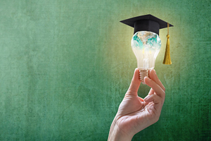 hand holding an illuminated lightbulb with a graduation cap on top