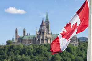 Canadian flag in the foreground with a castle surrounded by trees visible in the background 