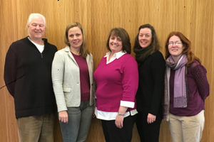 five people smile at the camera while standing arm-to-arm for a photo