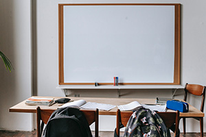 empty classroom with a blank whiteboard and a desk with papers and backpacks but no people