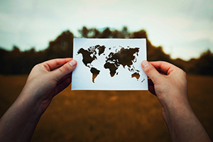 Two hands holding a cut-out photograph of the world.