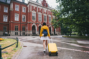 Individual walking towards an education building with luggage.