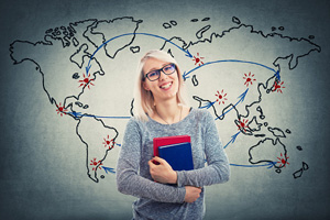 student holding books stands in front of a global map with flight path lines