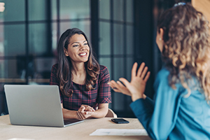 female interviewer sitting behind a laptop smiles while listening to a female interviewee