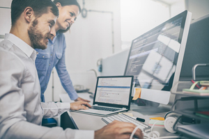 two smiling people working on computer code in office