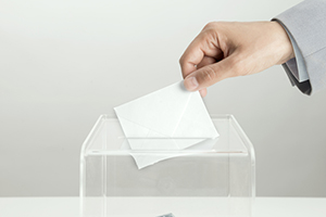 Hand inserting a ballot into clear box.