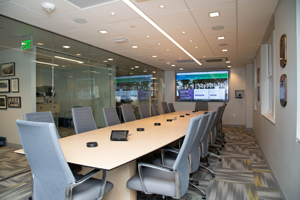 long conference table with empty chairs on either side and a TV screen on the wall