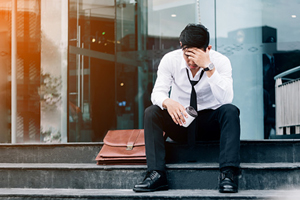 male in disheveled suit sits on a step with his head hung low