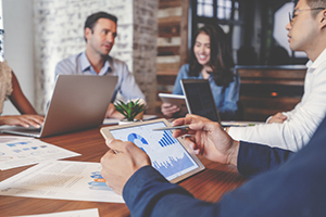 person sitting out of frame works on graphs on their tablet while sitting in a business meeting