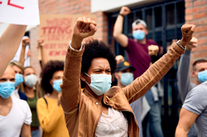 black woman wearing a mask, protesting with crowd of protesters