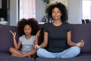 mother and daughter sit cross legged on a couch and meditate