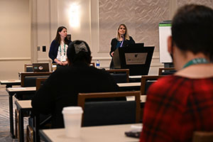 two female presenters speak from the front of an event space