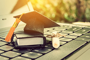 Graduation cap and diploma sitting on laptop keyboard.